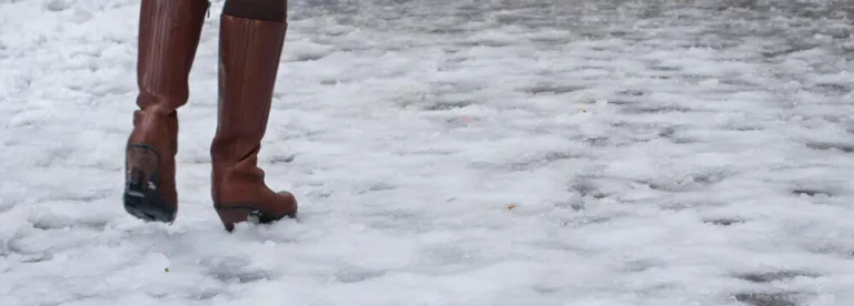 Person walking cautiously on a snow-covered, icy surface.
