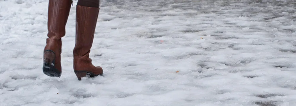 Person walking cautiously on a snow-covered, icy surface.