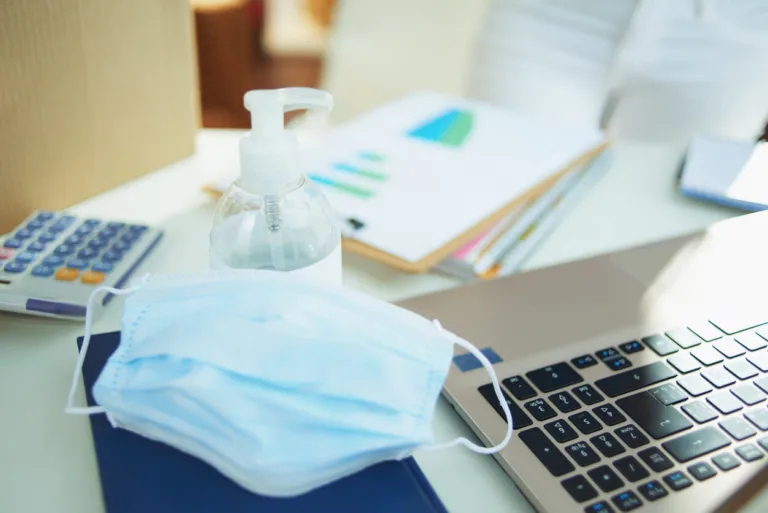 Office desk with mask, hand sanitizer and laptop.