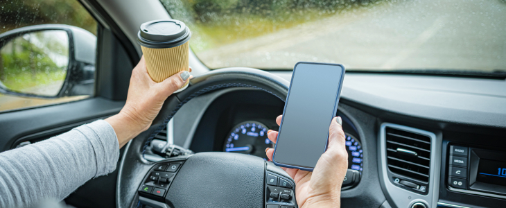 A person looking at her phone and drinking coffee while driving